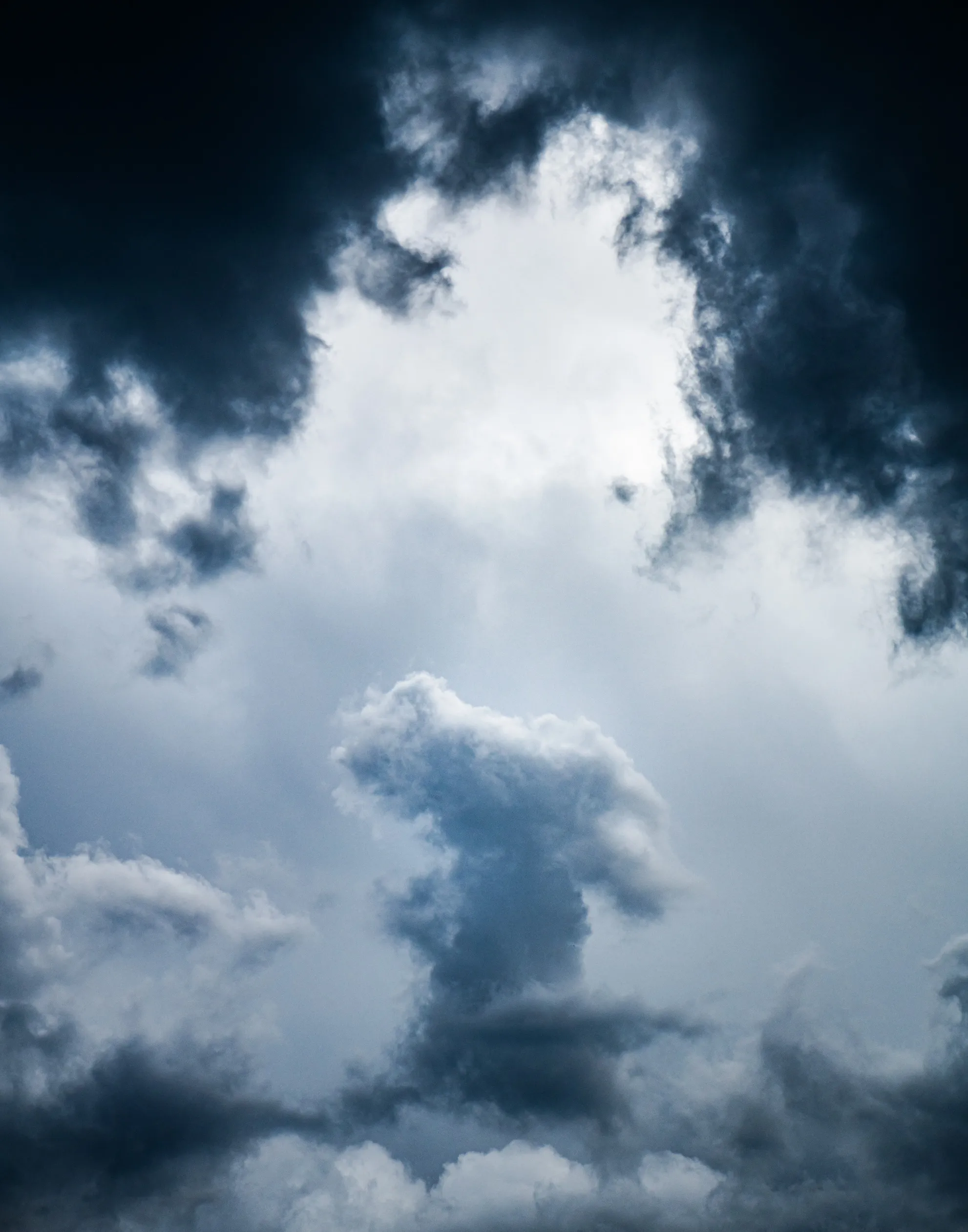 Dark storm clouds opening around a bright, towering white cloud