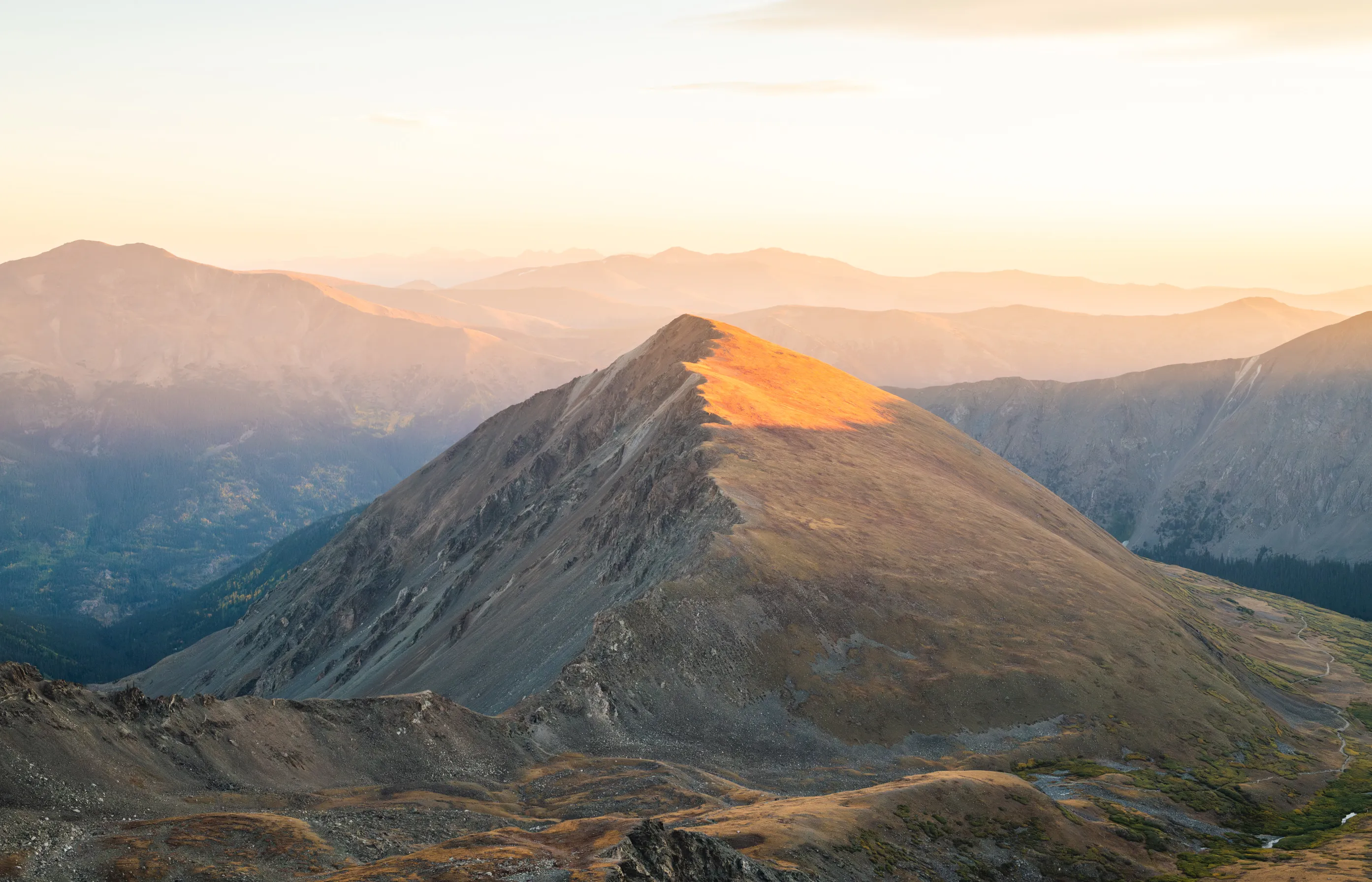 Warm early light catching the summit of a bare mountain peak above layered ridgelines