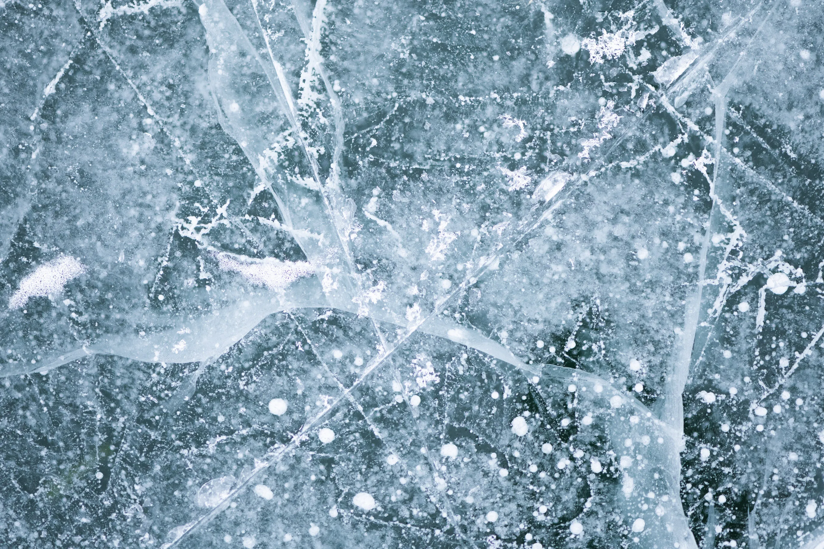 Cracks, bubbles and frost patterns in pale blue ice, seen from above