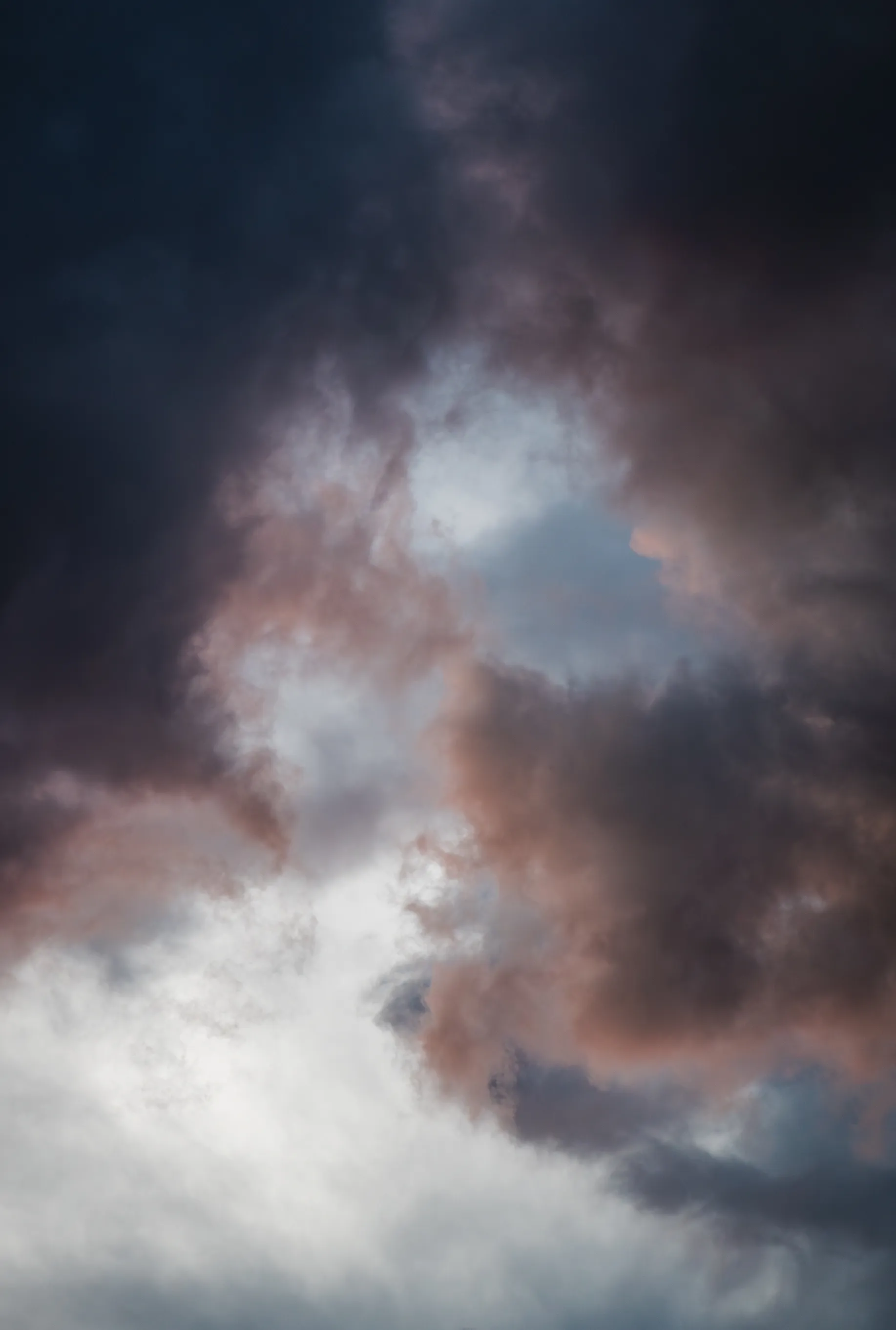 Dark, heavy clouds tinged with rose, light breaking through a gap at the center
