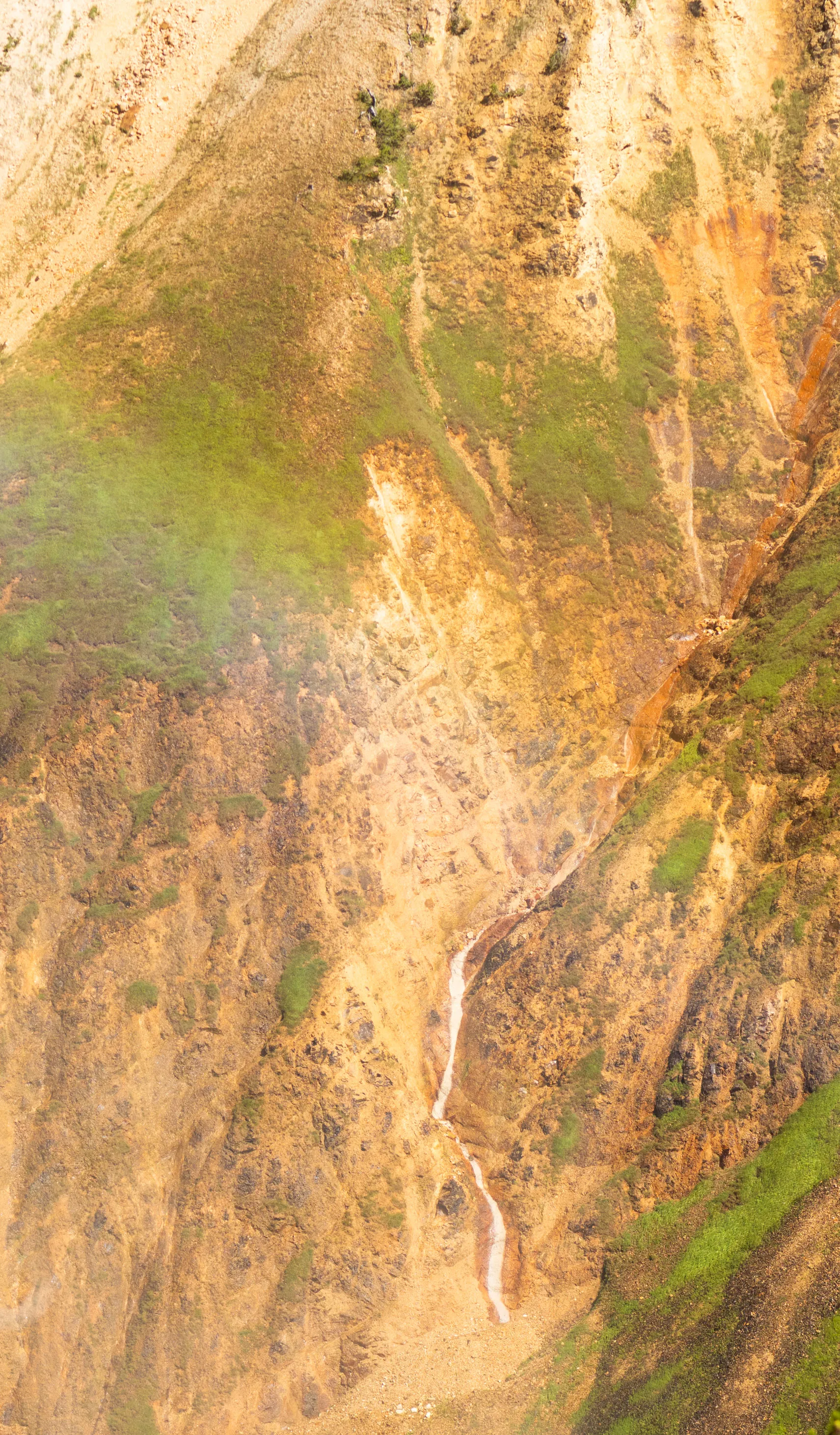 Steep yellow and ochre canyon walls with a thin waterfall and a faint rainbow in the mist